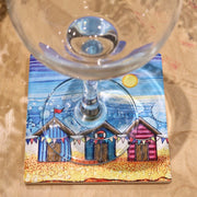 Beach Hut and Bunting ceramic coaster with wine glass on sandy surface showing full coastal scene
