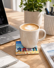 4 Beach Huts ceramic coaster on wooden desk with latte art coffee mug, laptop, notebook and plant