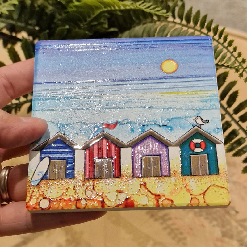4 Beach Huts ceramic coaster held in hand showing close-up of embossed beach hut design with glitter detail and sparkling textured sea