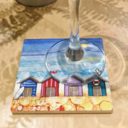 4 Beach Huts ceramic coaster with champagne flute on sandy surface showing full coastal scene with sparkling textured sea