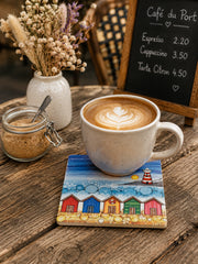 5 Beach Huts and Lighthouse ceramic coaster on wooden harbour café table with latte art coffee mug, dried flower arrangement, sugar jar and café menu board in background