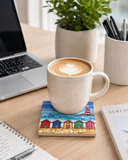5 Beach Huts and Lighthouse ceramic coaster on wooden desk with latte art coffee mug, laptop, notebook, plant and stationery