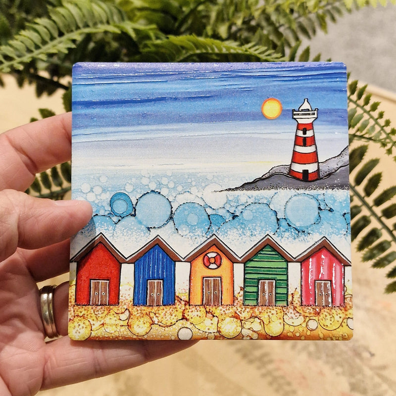 5 Beach Huts and Lighthouse ceramic coaster held in hand beside fern plant showing embossed detail and sparkling textured sea