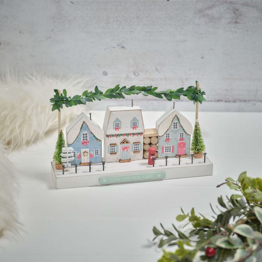 Cosy Cottage Lane wooden Christmas village street scene styled on a white surface with foliage and fur styling