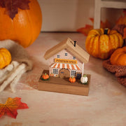 Pumpkin Spice café house wooden ornament with striped awning, painted windows, miniature pumpkins and chalkboard sign on a natural wood base, styled with autumn pumpkins and leaves