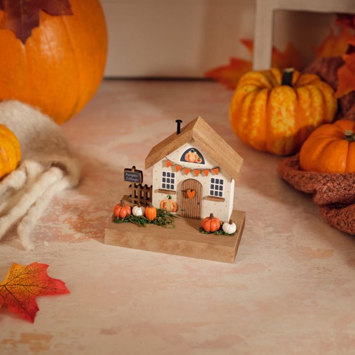 Pumpkin Cottage wooden house ornament with miniature pumpkins, orange bunting, small fence and Pumpkin Cottage sign on a natural wood base, styled with autumn pumpkins and leaves