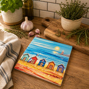 5 Beach Huts and Lighthouse ceramic trivet on wooden kitchen worktop beside herb pots, garlic and chopping board