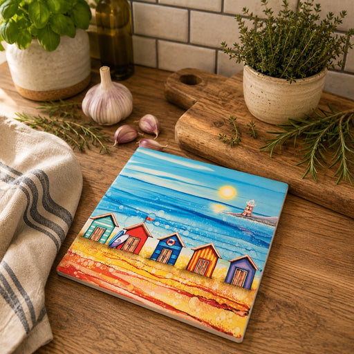 5 Beach Huts and Lighthouse ceramic trivet on wooden kitchen worktop beside herb pots, garlic and chopping board