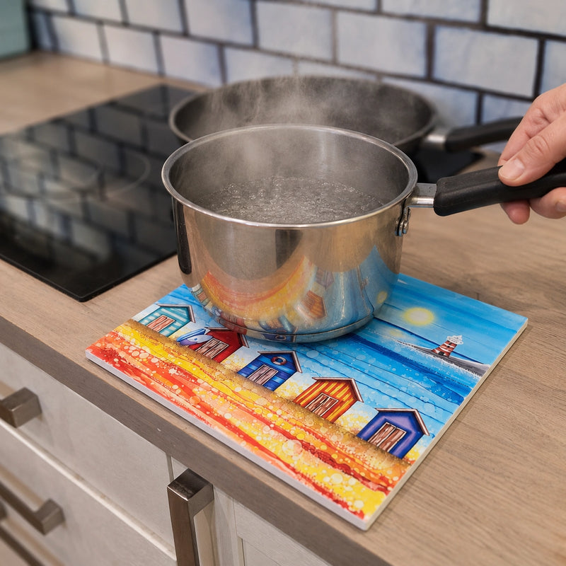 Boiling saucepan being placed on 5 Beach Huts and Lighthouse ceramic trivet on kitchen worktop beside induction hob