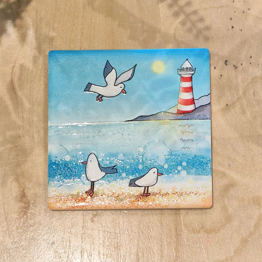 Seagull and Lighthouse ceramic coaster flat lay showing full coastal design on wooden surface