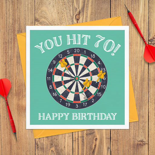 70th birthday card with a dartboard on a teal background with three yellow darts and the text "You Hit 70! Happy Birthday"