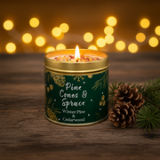 Pine Cones & Spruce Christmas candle tin lit with a warm glowing flame, styled on a rustic wooden surface with golden bokeh fairy lights and evergreen sprigs in a cosy festive setting