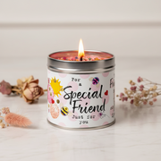 Special Friend candle tin lit with a warm glowing flame, styled on a light marble surface with soft neutral background and dried botanicals alongside