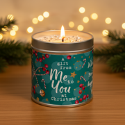 Me to You at Christmas candle tin lit with a warm glowing flame, styled against warm golden bokeh fairy lights in a cosy Christmas setting