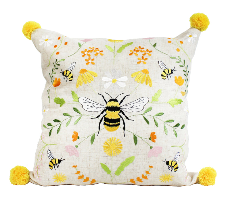 Bee Meadow Embroidered Cushion with large central embroidered bumblebee with yellow and black striped body and white wings, bee and meadow flower design in yellows and whites with green foliage on natural linen-mix background with yellow pom pom in each corner, 45 x 45 cm, on white background