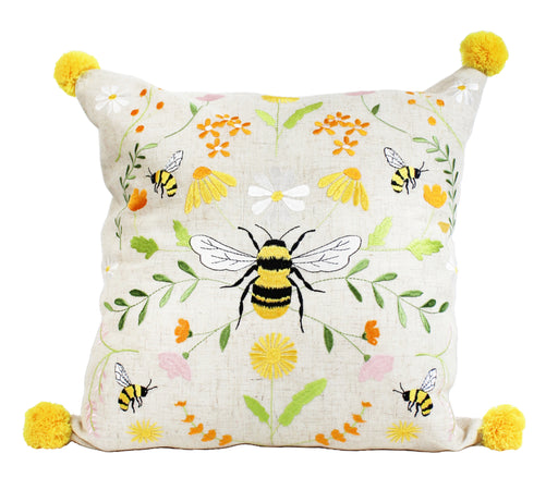 Bee Meadow Embroidered Cushion with large central embroidered bumblebee with yellow and black striped body and white wings, bee and meadow flower design in yellows and whites with green foliage on natural linen-mix background with yellow pom pom in each corner, 45 x 45 cm, on white background