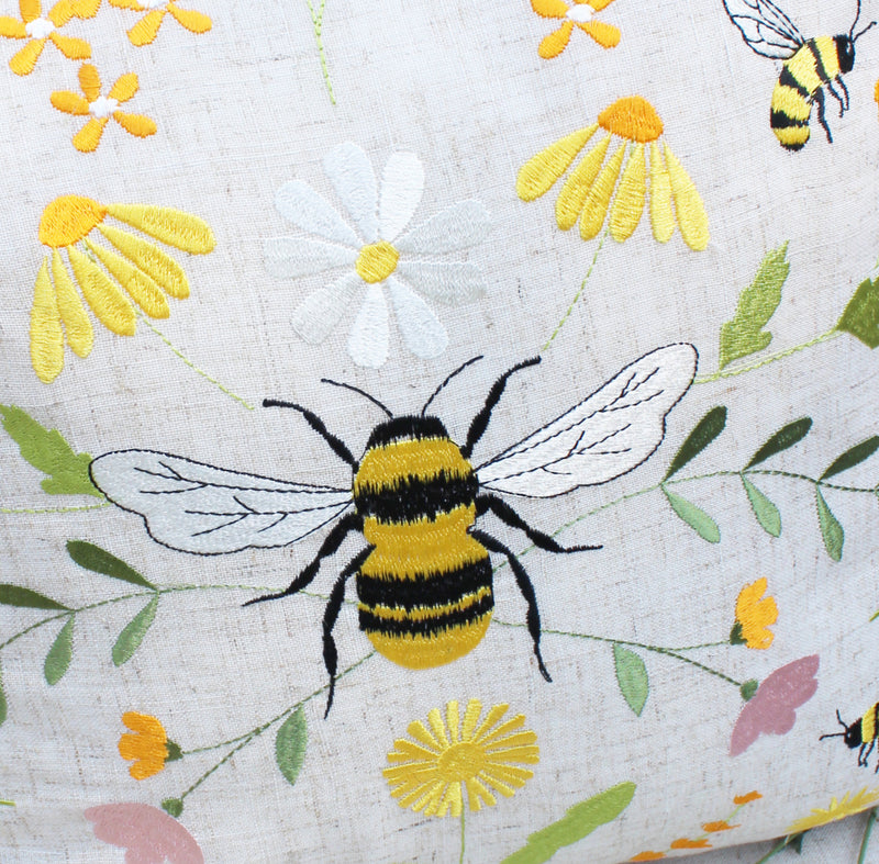 Bee Meadow Embroidered Cushion close-up showing large central embroidered bumblebee detail with yellow and black striped body and white wings, surrounded by meadow flowers in yellows and whites with green foliage