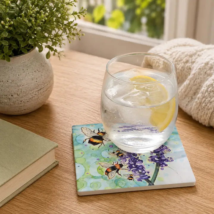 Bumblebee and Lavender ceramic coaster on wooden table with gin and tonic glass with lemon slice, beside plant and books