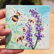 Bumblebee and Lavender ceramic coaster held in hand showing full bumblebee and lavender design with teal bubble-effect background