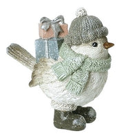 Christmas bird figurine with sparkly finish wearing a bobble hat and sage green scarf, carrying a stack of glittery gift boxes, standing in chunky boots