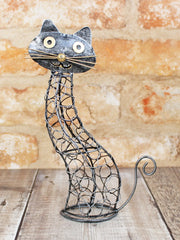 Open ironwork cat ornament handmade in Bali, twisted and looped wire body with flat metal head, gold-coloured eyes, nose and whiskers, curled wire tail, 22cm tall