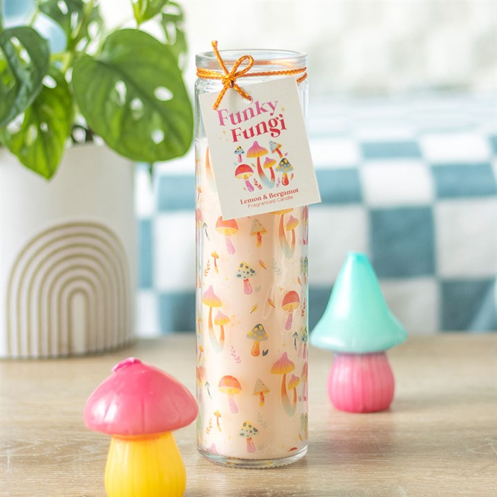 Funky Fungi Lemon & Bergamot tube candle in glass jar with orange twine bow and gift tag, styled on a wooden surface with colourful mushroom ornaments and a plant in the background