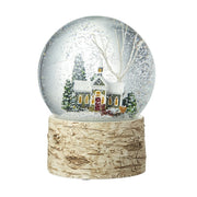 A church scene snow globe with a snow-covered church, evergreen trees and bare white branches inside a clear glass globe, on a natural birch bark-effect base