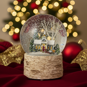 A church scene snow globe with a snow-covered church, evergreen trees and bare white branches inside a clear glass globe, on a natural birch bark-effect base in a festive setting