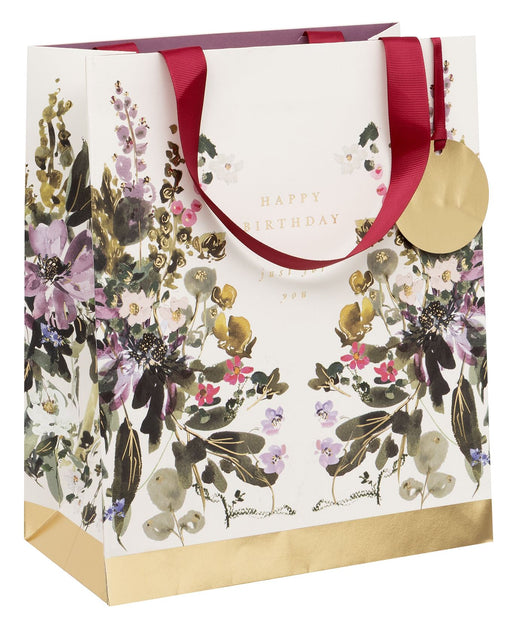 Stephanie Dyment Sunlit Harvest Large Happy Birthday Gift Bag with watercolour botanical print in purples, pinks and greens, gold foil accents, "Happy Birthday — just for you" in gold foil lettering, burgundy ribbon handles, gold foil base and circular gold gift tag on white background