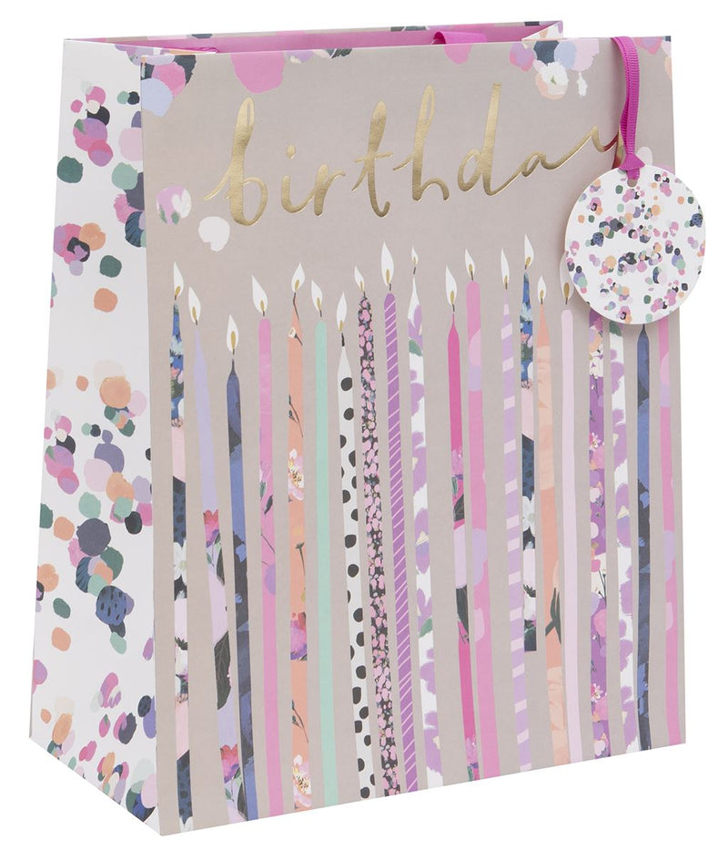 Stephanie Dyment Birthday Candles Large Gift Bag with row of patterned birthday candles in pinks, purples and pastels on soft taupe background, "birthday" in gold foil script, confetti dot side panel, fuchsia ribbon handles and circular confetti-print gift tag, 260 x 315 x 135 mm, on white background