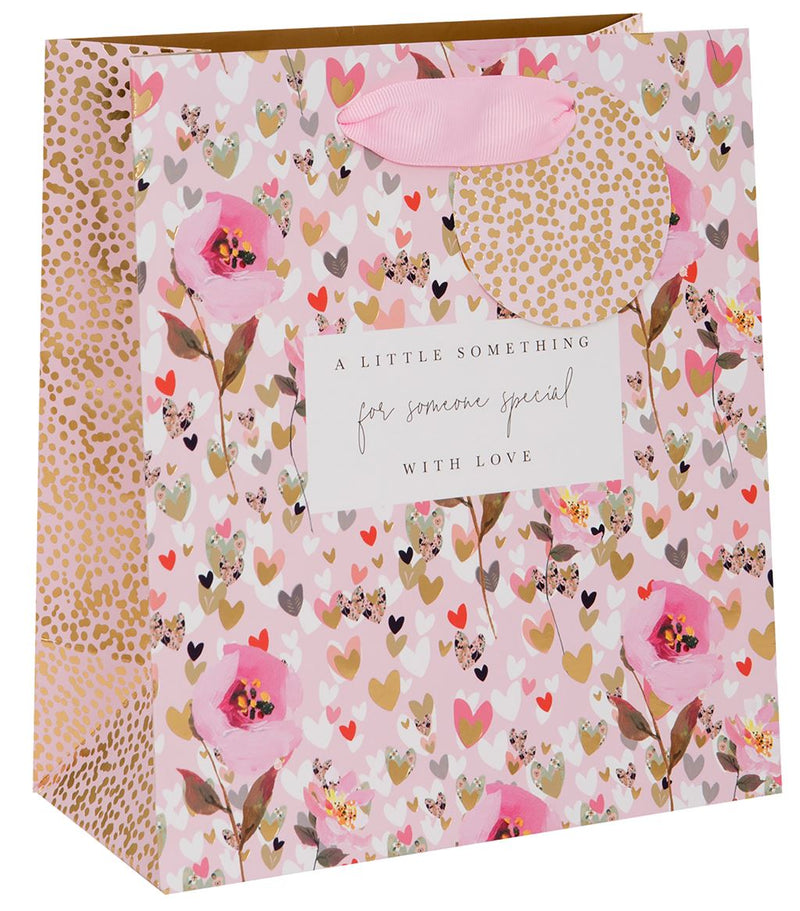 Stephanie Dyment Hearts and Flowers medium gift bag with pink floral and hearts design, gold foil dot accents, sentiment label and pink ribbon handles on white background