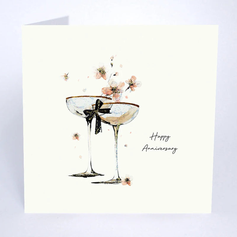 Happy Anniversary card by Five Dollar Shake, two champagne glasses with dark bow and scattered blossom on white background with glitter detail