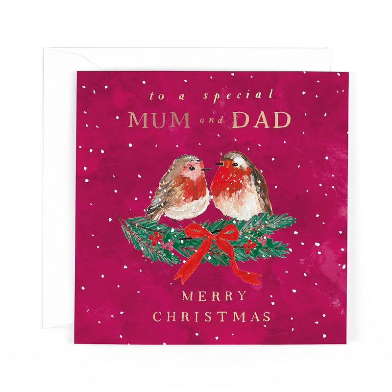 Special Mum and Dad Christmas card featuring two robins sitting together on evergreen branches decorated with berries and a ribbon bow, surrounded by falling snow.
