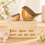 Robins appear when loved ones are near wood block on a light wooden surface with delicate flowers alongside and a soft neutral background