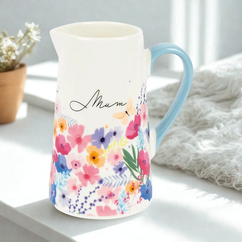 Meadow Mum bone china floral jug with wrap-around flower design and pastel blue handle, styled on a white shelf with a pot plant and white throw