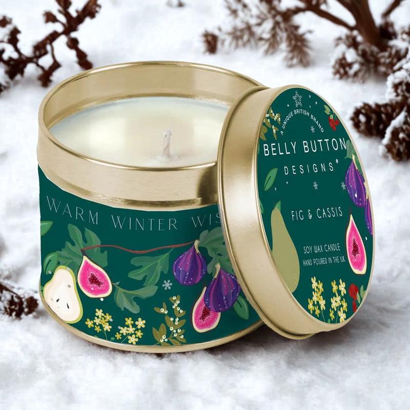 Belly Button Designs Warm Winter Wishes Fig & Cassis soy wax candle in dark green gold tin resting in snow with frosted pine branches