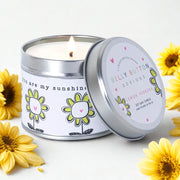 You Are My Sunshine lemon verbena soy wax lit candle in recyclable tin with lid leaning against it, surrounded by yellow sunflowers on a styled background