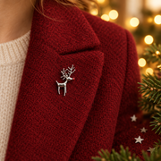 Rhodium plated standing reindeer brooch pinned on a deep red knitted jacket lapel,  surrounded by silver star confetti and evergreen sprigs with warm golden bokeh fairy lights in the background