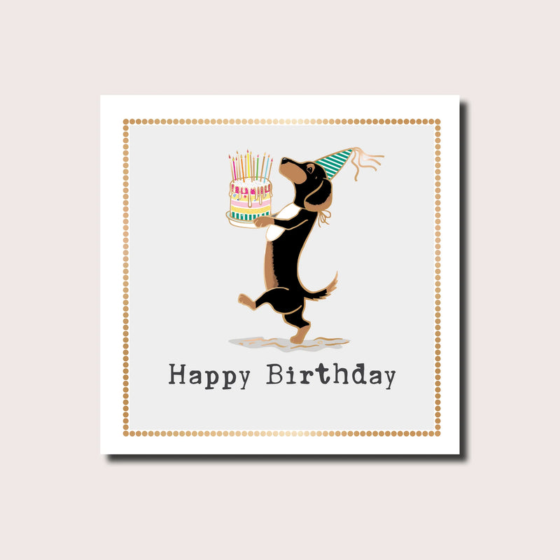Happy birthday card featuring a dachshund in a party hat presenting a candle-topped birthday cake, gold dot border, gold foil finish, blank inside, square format 155 x 155mm