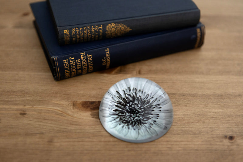Dahlia glass paperweight styled on a wooden surface alongside a stack of vintage hardback books