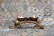 Woodland bird double tealight holder with lit tealight candles, two birds on a curved branch with pine cone cups, styled on a floral surface