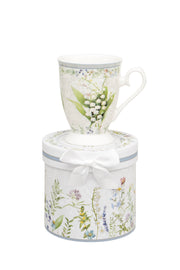 Snowdrop Mug in Gift Box footed mug with snowdrop print sitting on top of a matching cylindrical gift box with wildflower meadow design and white ribbon bow on white background