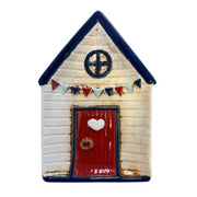 Beach Hut Ceramic Trinket Dish front view showing cream ceramic beach hut shape with navy pointed roof, circular porthole window, red door with heart detail and ring knocker, bunting garland across front, on white background