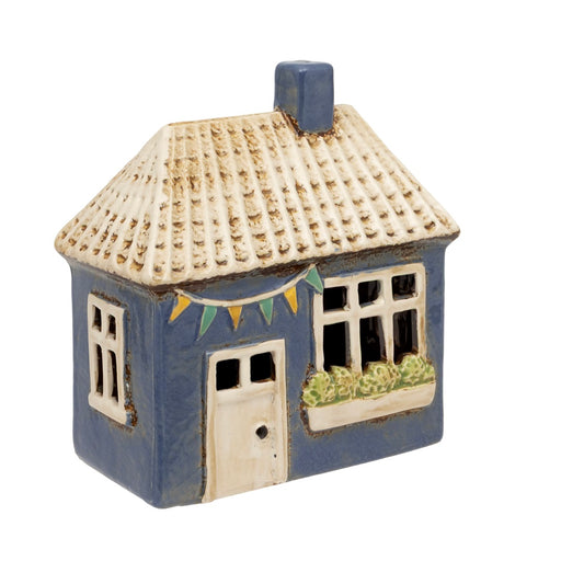 Lily Cottage Tealight Holder, blue ceramic cottage with textured cream tiled roof, blue chimney, flower window box, bunting garland and white door, warm glow through windows, on white background
