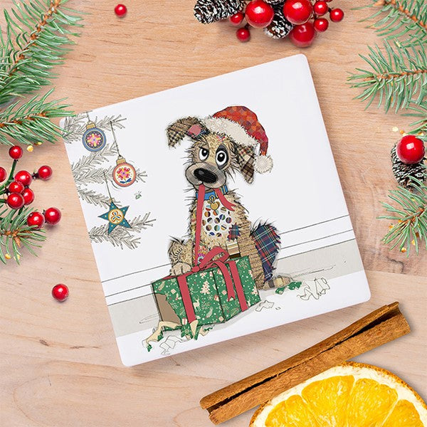 Bug Art Christmas dog coaster featuring a characterful scruffy dog in a Santa hat sitting next to a wrapped gift by a Christmas tree, styled on a wooden surface with festive foliage⠋