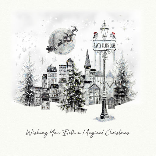 A shimmering illustrated Christmas card showing a snowy cityscape with a Santa Claus Lane street lamp, two robins in Santa hats, twinkling Christmas trees, and Santa's sleigh flying past a full moon, with the sentiment "Wishing You Both a Magical Christmas"
