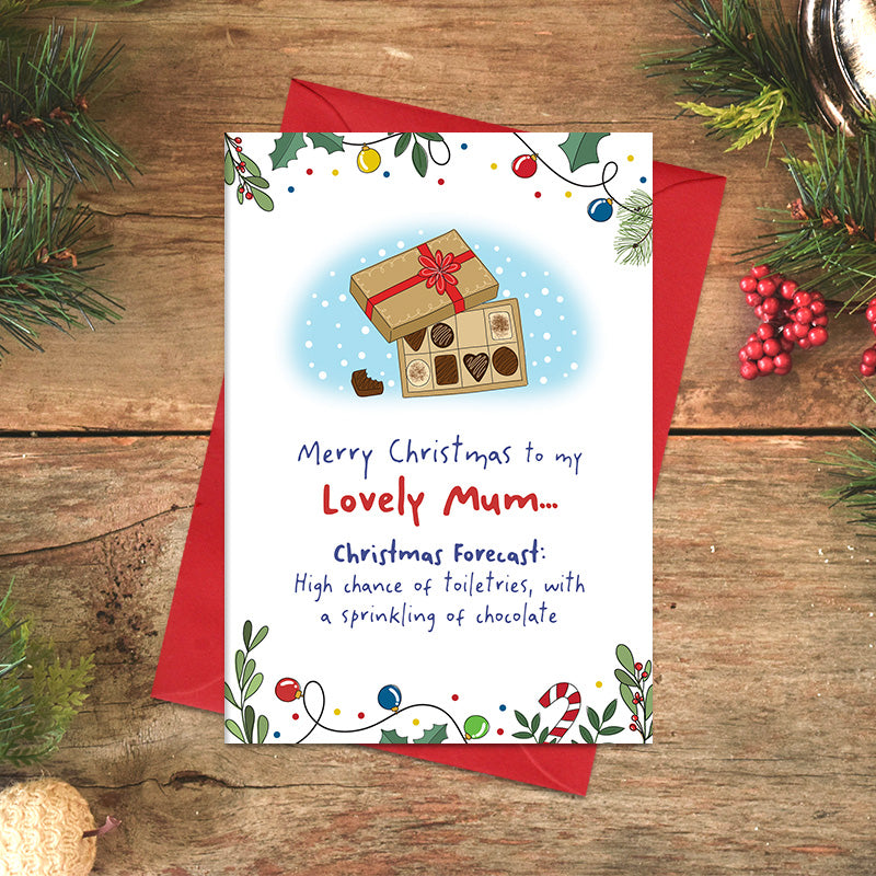Lovely Mum Christmas card featuring an illustrated box of chocolates and the joke ‘Christmas forecast: High chance of toiletries, with a sprinkling of chocolate’, framed by festive foliage and baubles.