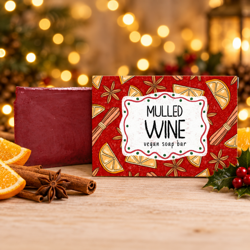 Neon Magpie Mulled Wine Vegan Soap Bar in burgundy festive packaging styled on a pale wooden surface with cinnamon sticks, star anise, orange slices and holly, warm golden bokeh background