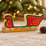 Wooden Christmas sleigh toy beneath Christmas tree branches beside a pinecone and warm fairy lights