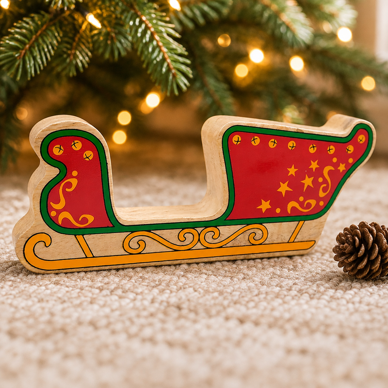 Wooden Christmas sleigh toy beneath Christmas tree branches beside a pinecone and warm fairy lights